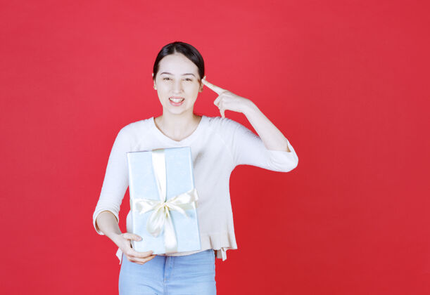 手势微笑的年轻女子拿着礼品盒 手指着她的头女人礼物脸