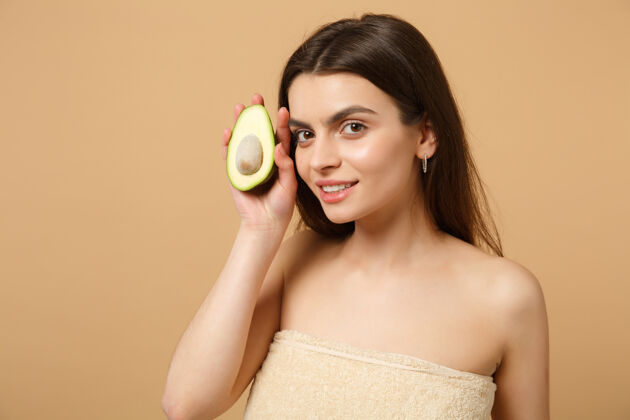素食特写黑发半裸女人完美的皮肤裸妆举行鳄梨隔离米色粉彩墙上健康蔬菜清晰