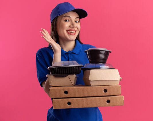 请穿着制服的漂亮送货员举手站着 手里拿着比萨饼盒上的食品包装和容器食物拿着盒子