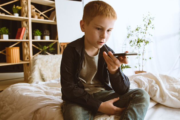 科技男孩在家里使用不同的小玩意带智能手表 智能手机或平板电脑和耳机的小模型自拍 聊天 玩游戏 看视频孩子和现代科技的互动生活方式童年男孩