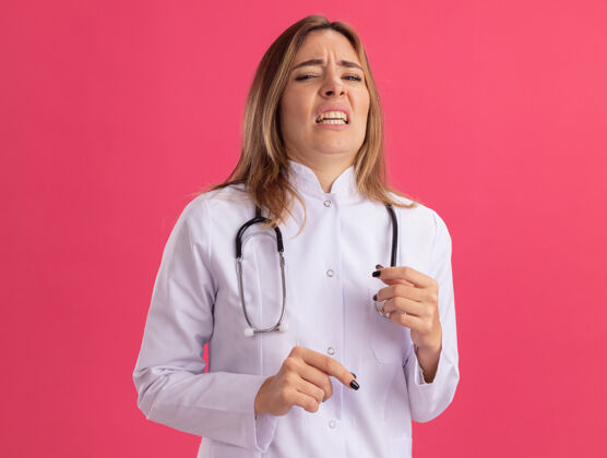 衣服穿着医用长袍的神经质年轻女医生 听诊器被隔离在粉红色的墙上公民尖叫医生