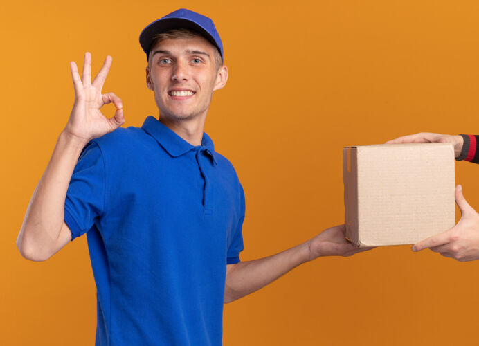 给予年轻的金发送货员微笑着把名片盒递给某人 并示意“ok”手势年轻橙色卡片盒