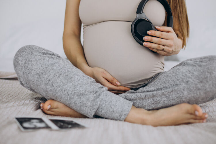 母亲孕妇带着超声波照片把带音乐的耳机放在肚子上为人父母人健康