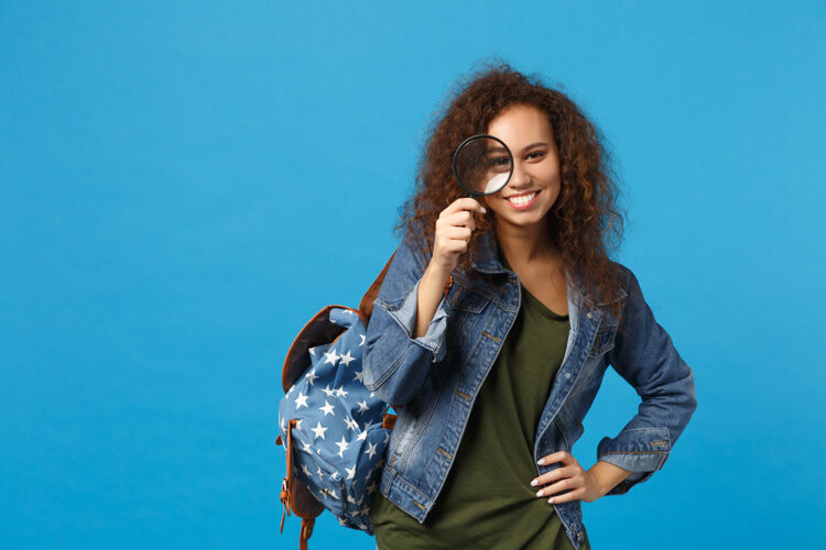 包年轻的非洲裔美国女孩十几岁的学生在牛仔服装 背包举行的蓝色墙上孤立的时钟民族站立女人