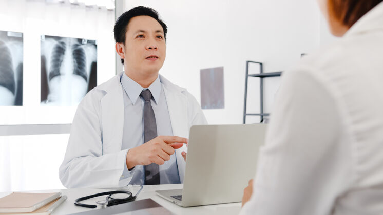 办公室严肃的亚洲男医生穿着白色医疗制服 用笔记本电脑发表精彩的新闻谈话 讨论结果检查讨论女性