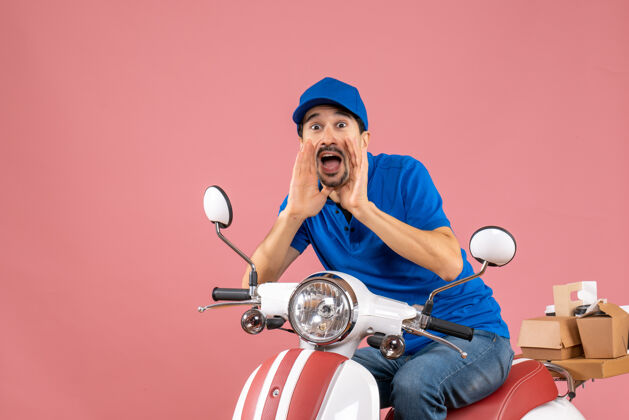 男性前视图的情感信使家伙戴着帽子坐在滑板车上 并呼吁在粉彩桃色背景的人摩托车前面呼叫
