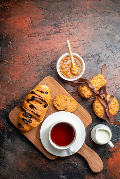咖啡俯瞰美味的克罗伊桑特一杯红茶放在木质砧板上蜂蜜饼干牛奶堆在黑暗的表面木板风景早餐