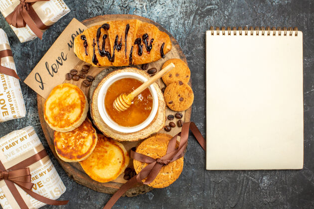 曲奇俯瞰美味的早餐 羊角面包 薄饼 饼干 蜂蜜 为心爱的人准备的漂亮礼物 以及黑色背景上的螺旋面书堆栈头顶背景