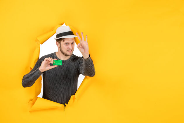 帽子顶视图微笑的家伙持有银行卡 并显示三个在一个撕破的黄色墙壁帽子头盔工作