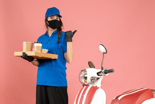 手套俯视图：戴着医用口罩手套的快递员女孩站在摩托车旁 手里拿着咖啡小蛋糕 背面是粉色背景医疗人小