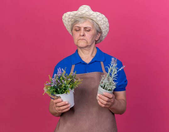 花园自信的上了年纪的女园丁戴着园艺帽拿着花盆看抱老人自信