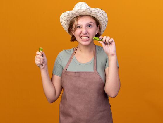 磨损恼怒的年轻斯拉夫女园丁戴着园艺帽 手里拿着一部分碎辣椒坏的热的花园