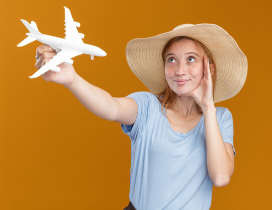 飞机戴着沙滩帽 满脸雀斑的年轻红发姜姑娘高兴地把手放在脸上 举着飞机模型抬头看向上海滩脸