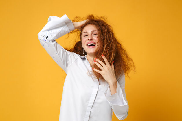 一个笑着的年轻红发女 穿着白衬衫 孤零零地站在黄橙色的墙上显示白种人休闲