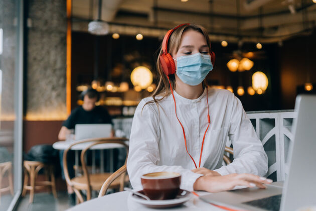 咖啡一个戴着耳机坐在咖啡店里的女孩冠状病毒爆发了病毒耳机咖啡馆