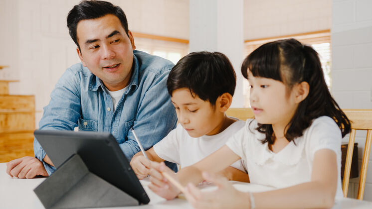 工作快乐亚洲家庭家庭教育 爸爸教孩子在家客厅使用数码平板电脑一起小桌子