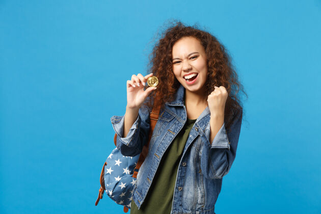 支付年轻的非裔美国少女 穿着牛仔服 背包里装着比特币 孤零零地站在蓝色的墙上黄金支付民族