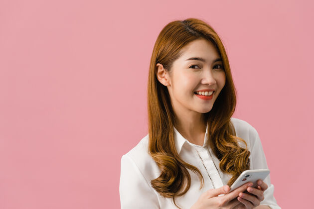 女士惊讶的亚洲小姐用手机积极的表情 笑容灿烂 穿着休闲服 看着粉色背景的相机年轻电话商务女性