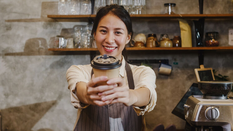 业主照片：年轻的亚洲女咖啡师女服务员拿着咖啡杯 在城市咖啡馆感觉很开心女士工作杯子
