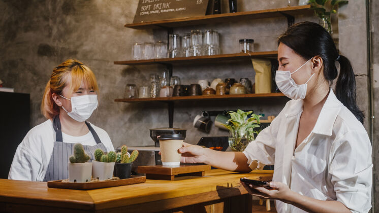 外卖年轻的女咖啡师戴着口罩在咖啡厅为顾客端上热咖啡纸杯业主小厨师