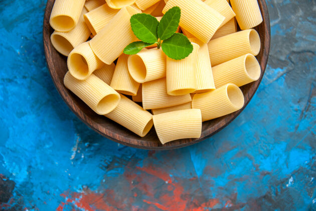 碗准备晚餐的半张照片 蓝色背景的棕色锅里放着绿色的意大利面一半传统晚餐