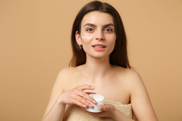 包装近景半裸体女人完美皮肤裸妆涂抹面霜隔离在米色粉彩墙上面部治疗健康