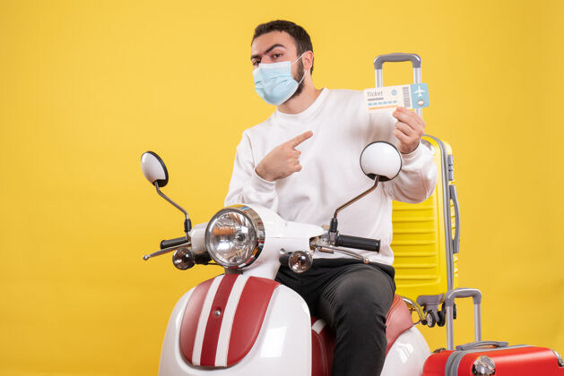 旅行旅行概念的俯视图 戴着医用面罩的年轻人坐在摩托车上 黄色手提箱放在上面 指着车票坐人运动