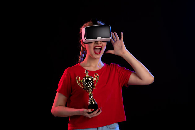 赢家在黑暗的墙壁上 年轻女性正在玩虚拟现实和冠军杯黑色肖像年轻女性
