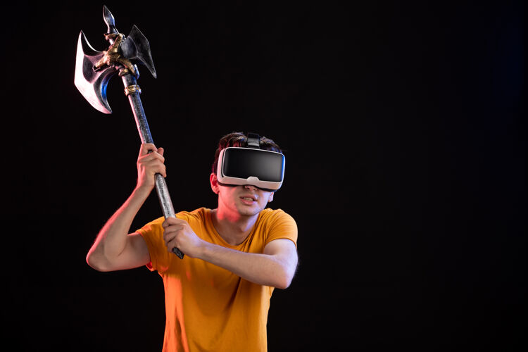 人在黑暗的墙上 年轻人拿着战斧玩虚拟现实的画像虚拟现实肖像人