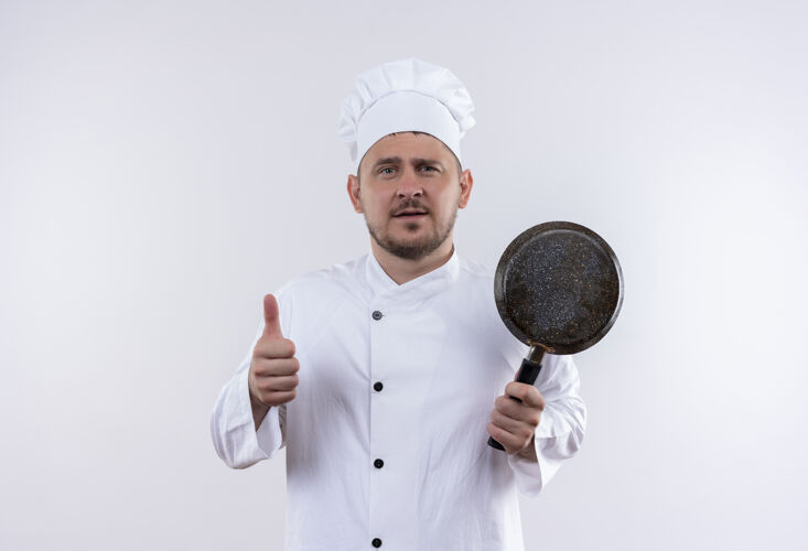 年轻自信的年轻帅哥厨师 身着厨师制服 手拿煎锅 孤立地在白墙上竖起大拇指拿着薯条厨师