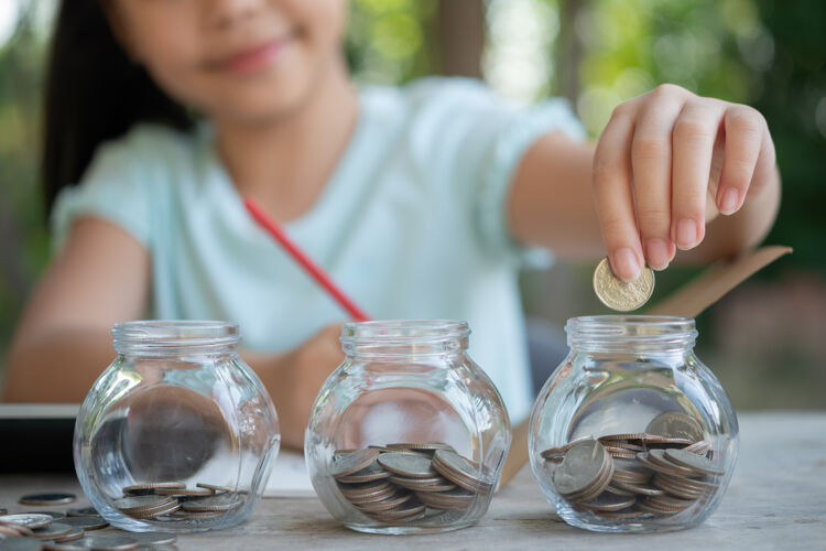 手可爱的亚洲小女孩玩着硬币堆成一堆的钱 孩子把钱存进存钱罐 存进玻璃罐孩子数着自己存的硬币 孩子们学习着关于未来的概念硬币教育股票