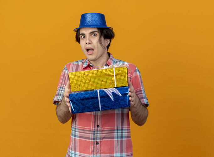 复制印象深刻的白人帅哥戴着蓝色派对帽拿着礼盒橙色盒子蓝色