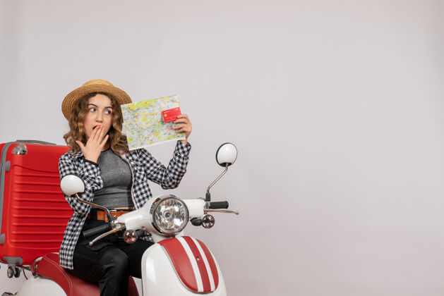 摩托车骑着轻便摩托车的年轻女子拿着灰色的卡片和地图 大吃一惊摩托车人地图