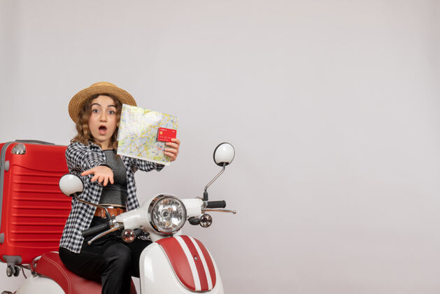 地图骑在轻便摩托车上的年轻女子拿着灰色的卡片和地图 心里很奇怪灰色摩托车时尚