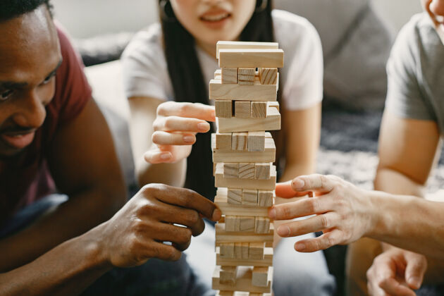 沙发非洲男孩和亚洲夫妇玩詹加玩棋盘游戏在一个自由的时间集中在一个游戏大厅衣服玩