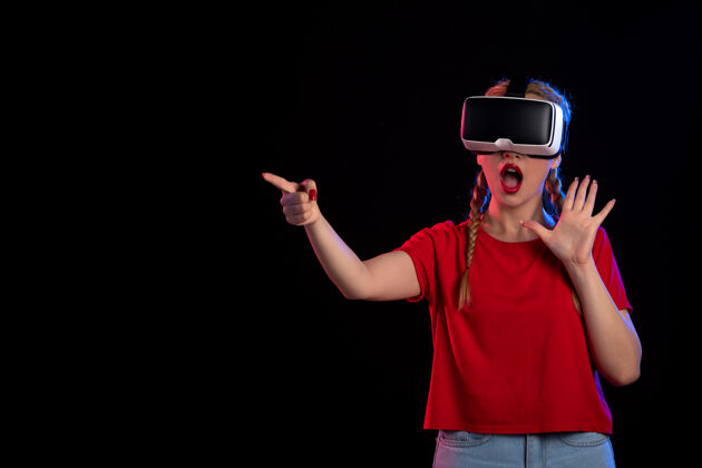 虚拟现实年轻女性在黑暗的墙上玩虚拟现实的正面图正面年轻女性成人