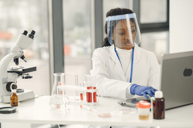 生物化学血液实验室研究 冠状病毒概念美国妇女检查血液和使用笔记本电脑黑发人非洲化学