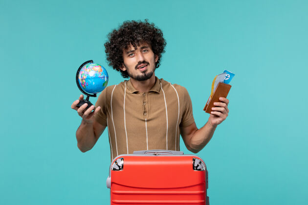 成人前视图度假男子拿着地球仪和浅蓝色的机票假期地球仪旅行