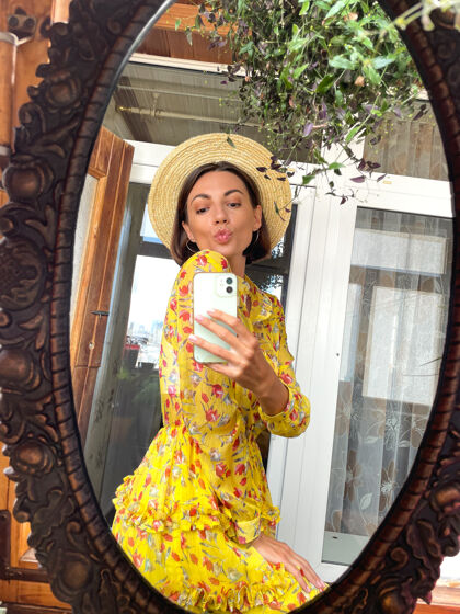 自信家里的美女穿着亮黄色的夏装 戴着帽子 用手机在镜子里自拍故事 在社交媒体上发帖社交夏天电话
