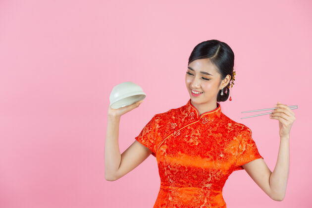 空美丽的亚洲女人快乐的微笑和吃在粉红色背景的中国新年筷子复制空间中国人