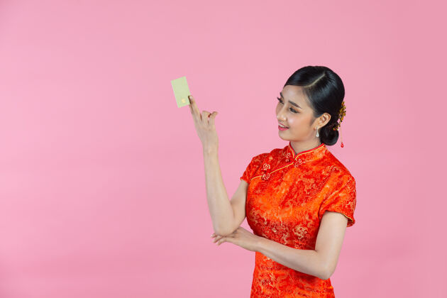 亚洲美丽的亚洲女人开心的微笑 在粉色背景上展示中国新年的信用卡微笑东方展示