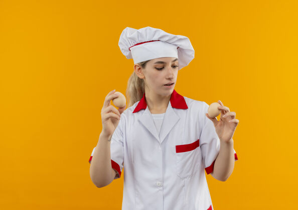 年轻年轻漂亮的厨师穿着厨师制服 手里拿着鸡蛋 看着隔离在橙色墙上的鸡蛋厨师鸡蛋漂亮