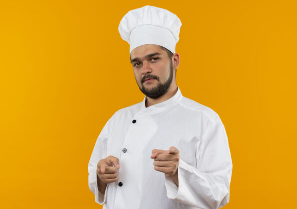 烹饪自信的年轻男厨师穿着厨师制服 在橙色的墙上做着孤立的手势 留着复制空间年轻男性自信
