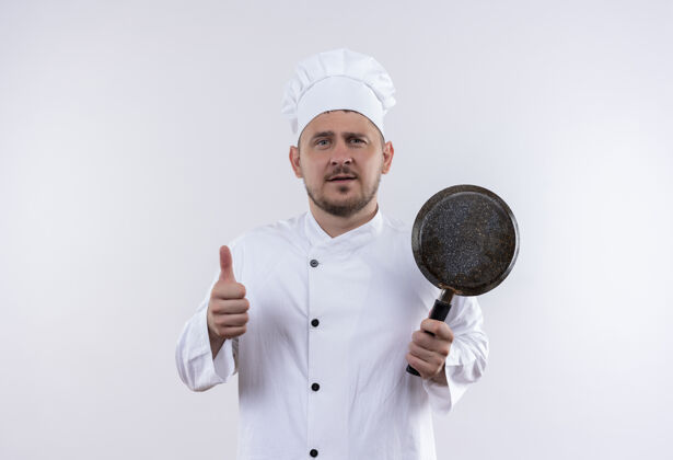 年轻自信的年轻帅哥厨师 身着厨师制服 手拿煎锅 孤立地在白墙上竖起大拇指拿着薯条厨师
