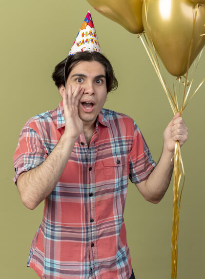 男人戴着生日帽的白人帅哥兴奋地把手放在嘴边 手里拿着氦气球氦绿色帅气