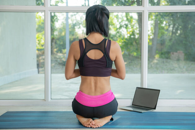 训练年轻的瑜伽女士练习瑜伽 做运动 坐着摆姿势 锻炼 穿着运动服 在笔记本电脑上看在线健身视频教程 坐在家里锻炼锻炼教练女性
