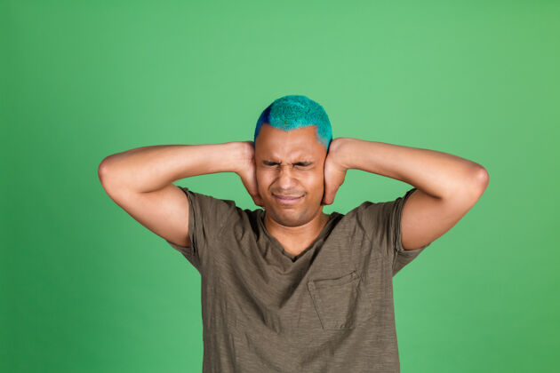 压力一个穿着休闲装的年轻人在绿墙上用手捂住耳朵噪音发光手势