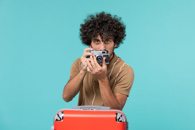 行李带着红色手提箱的度假男人用蓝色的相机拍照旅行蓝色照片