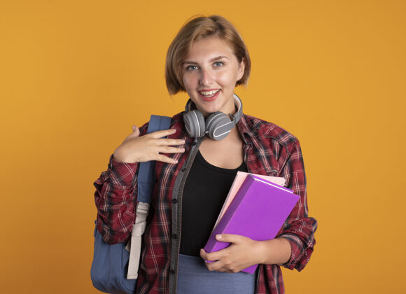 穿微笑着的年轻斯拉夫女学生戴着耳机背着书包拿着书和笔记本笔记本微笑复制