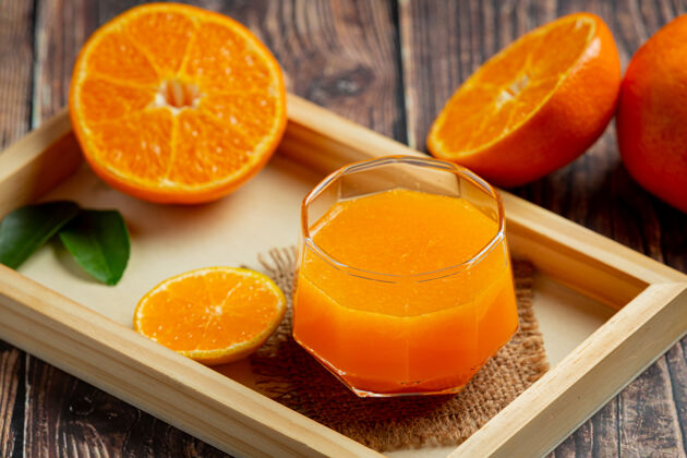 叶子新鲜的橙汁在黑暗的木制背景玻璃鸡尾酒挤压一半